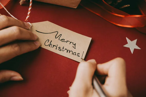 ギフト用タグにメリー クリスマスを書く女性の手 — ストック写真