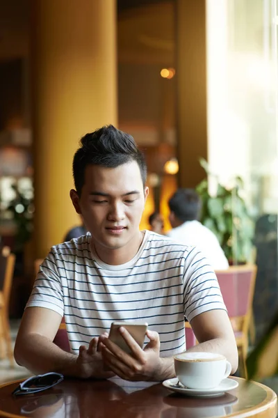 在咖啡馆里喝咖啡的年轻女人检查他的智能手机 — 图库照片