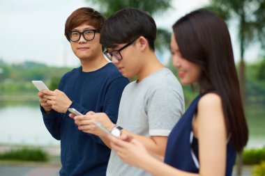Korean teenagers using applications on smartphones when standing outdoors clipart