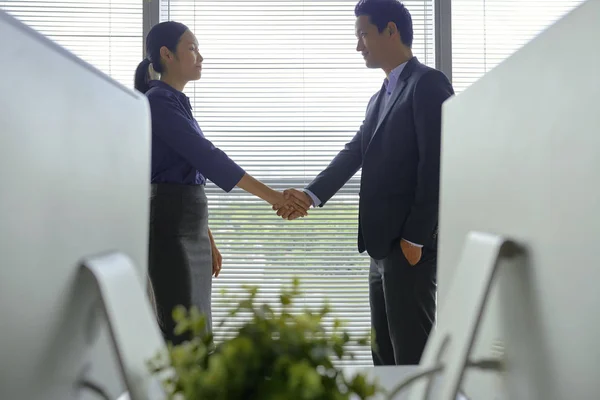 Young Asian business people shaking hands and having productive meeting in office