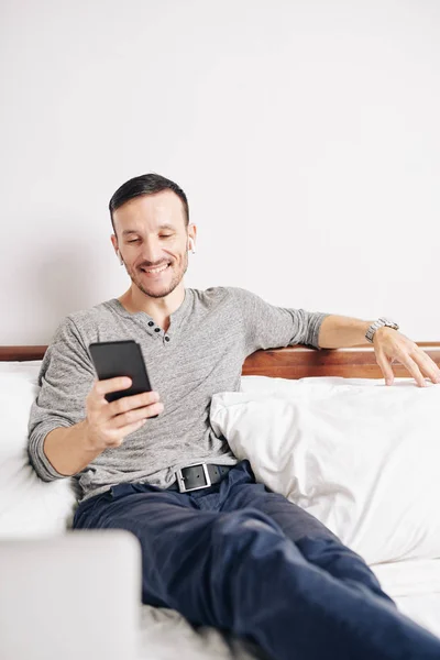 Smiling Cheerful Young Man Sitting Bed Reading Funny Messages Friends — Stock Photo, Image