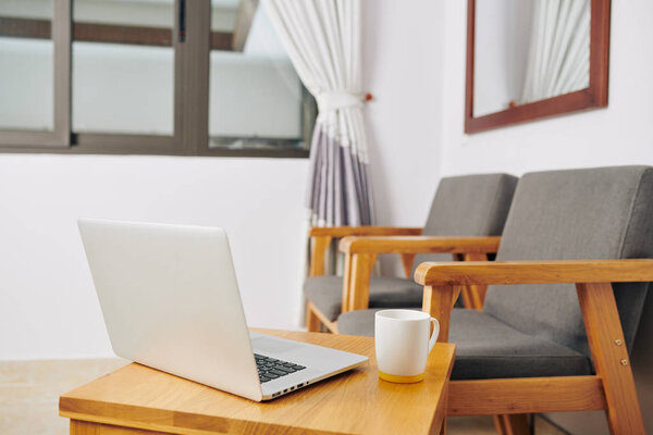 Room with two empty armchairs and small table with cup of coffee and opened laptop