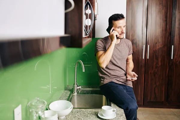 Przystojny Młodzieniec Siedzi Blacie Kuchennym Rozmawia Przez Telefon Zamawia Pizzę — Zdjęcie stockowe