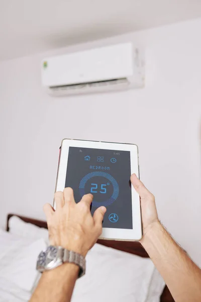 人类的手在平板电脑上使用气候控制应用程序来调节房间的温度 — 图库照片