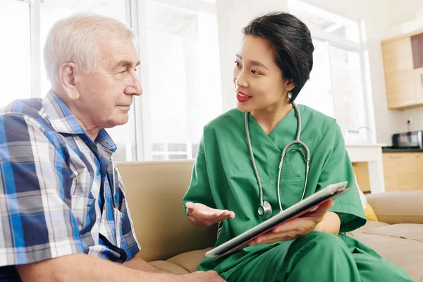 Usmívající Pracovnice Nemocnice Navštěvující Seniorského Pacienta Doma Ukazující Informace Tabletu — Stock fotografie