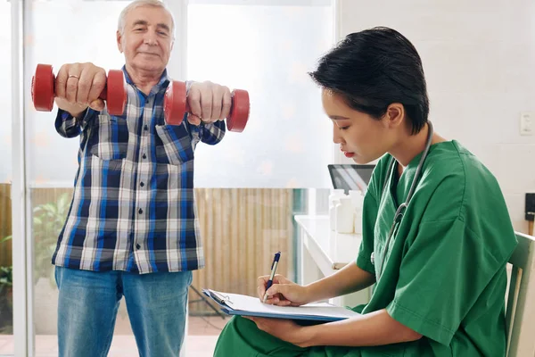 Sorrindo Homem Sênior Fazendo Exercícios Com Dumbbells Quando Enfermeira Tomar — Fotografia de Stock