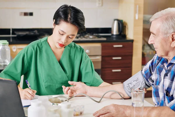 Serious Young Asian Nurse Measuring Blood Pressure Filling Medical Card — Stock Photo, Image