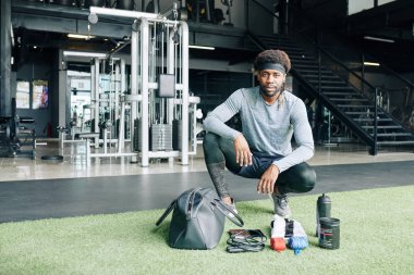 Siyah adam spor çantasını atlama ipi, bandaj, akıllı telefon ve spor gıdasıyla boşaltıyor.