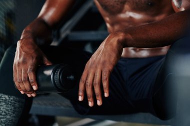 Basamaklarda plastik su şişesiyle oturan ve yoğun bir eğitimden sonra dinlenen sağlıklı genç adamın kırpılmış görüntüsü.