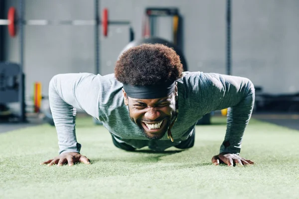 Handsome young Black man struggling with doing push-ups on gym floor