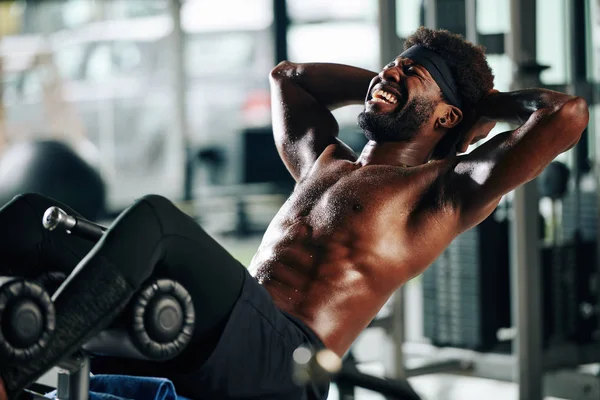 在健身房的长椅上做仰卧起坐的情绪汗流浃背的肌肉男人 — 图库照片