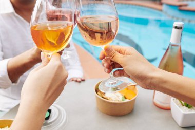 Açık havuz partisinde eğlenirken gül şarabı içen insanların yakın plan görüntüleri.