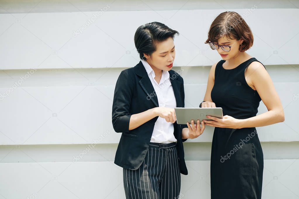Serious businesswomen pointing at screen of tablet computer and discussing important article
