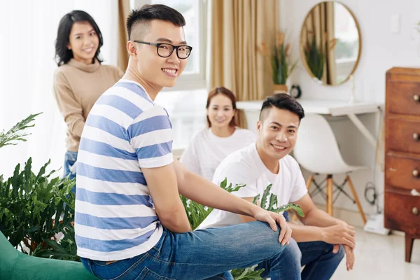 Cheerful young Asian man in glasses spending time with friends at home