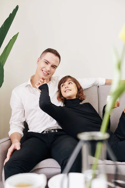 一对积极的白人年轻夫妇躺在舒适的沙发上喝茶的画像 — 图库照片