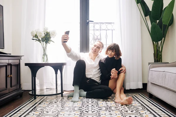 Joven Alegre Sentado Suelo Casa Con Novia Tomando Selfie — Foto de Stock