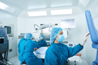 Ameliyat odasındaki cerrahi ekipman için önlüklü Asyalı hemşire program ayarlıyor.