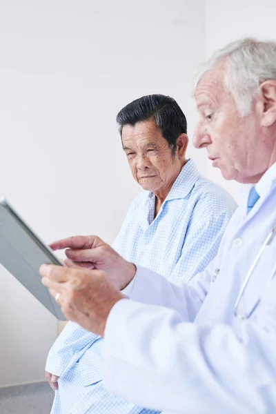 一般開業医は 高齢患者へのタブレットコンピュータ上の医療検査結果を示す — ストック写真