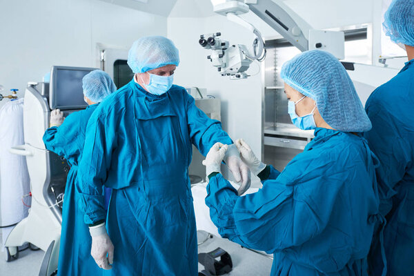 Assistant helping surgeon to wear latex gloves when standing in operating room