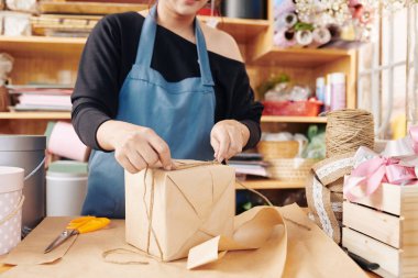 Çiçekçi dükkanında paketlenmiş hediye kutusunu kordonla bağlarken çekilmiş bir resim.