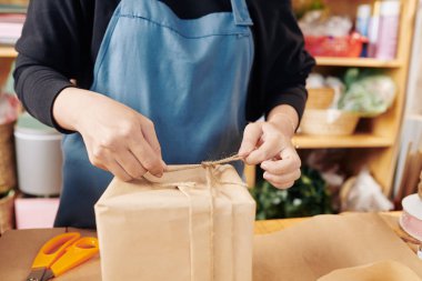 Çiçekçinin elleri hediye kutusuna ip bağlayıp fiyonk yapıyor.