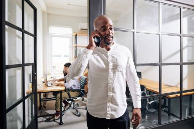 Beyaz gömlekli olgun bir girişimci iş ortağıyla konuşmak için ofis odasından çıkıyor.