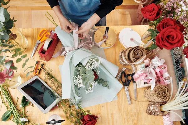 Florist tying ribbon of beautiful bouquet of flowers, view from above