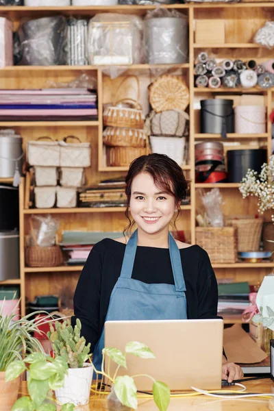 Lovely young flower shop worker accepting online orders via program on computer