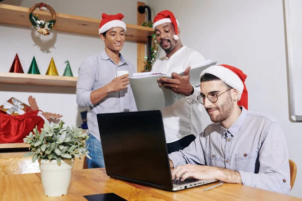 Meslektaşları Dosyada Belgeleri Tartışırken Noel Baba Şapkalı Genç Adam Ofiste — Stok fotoğraf