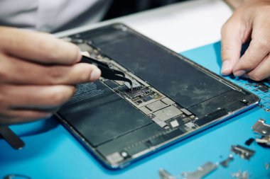 Tablet bilgisayarına mikroçip yerleştirmek için cımbız kullanan tamircinin yakın plan resmi