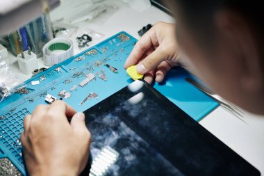 Dijital tablet ekranını kaldırmak ve iç bileşenleri kontrol etmek için gitar penası kullanan tamircinin elleri