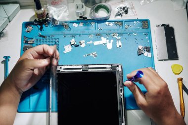Masasındaki tablet bilgisayarını kaldırırken cımbız ve tornavida kullanan tamirci, yukarıdan görünüm
