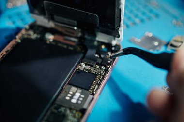 Close-up image of smartphone repairman using tweezers to remove antenna cable when trying to get access to the speaker clipart