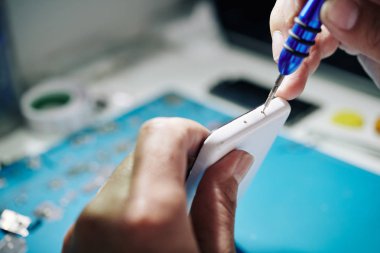 Akıllı telefonun alt kenarındaki pentalobe vidalarını söken tamircinin yakın plan görüntüsü