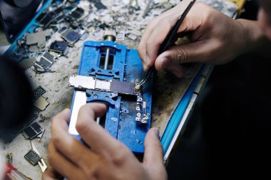 Akıllı telefonun mantık panosuna lehim yapıştırıcısını uygulamak ya da kaldırmak için cımbız kullanan tamirci