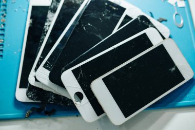 Tamirci masasında kırılmış ya da kırılmış akıllı telefon ekranları, yukarıdan görünüm