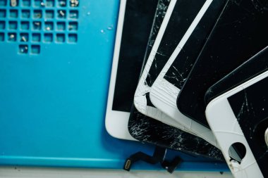 Birçok kırık ve kırılmış akıllı telefon ekranı tamir atölyesindeki masada.