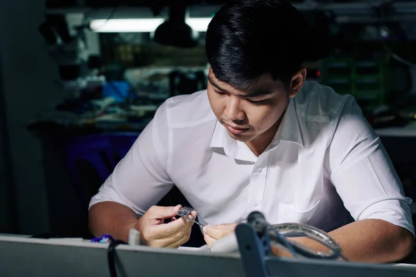 Pensive Young Asian Repairman Looking Smartphone Logic Board His Hand — Stock Photo, Image
