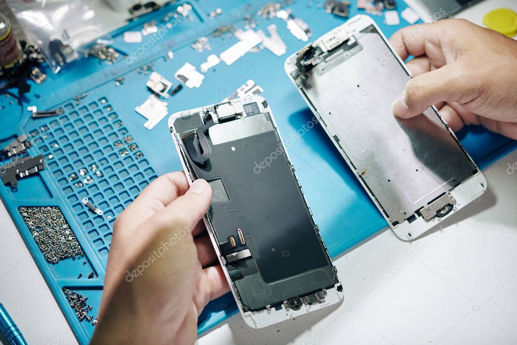 Hands of repairman replacing broken screen of smartphone