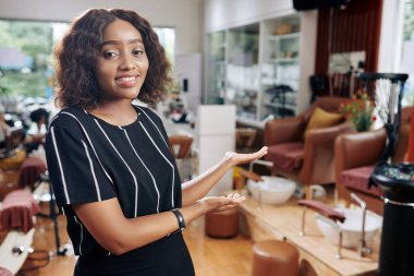 Beautiful young hair salon owner making welcoming gesture to invite customers
