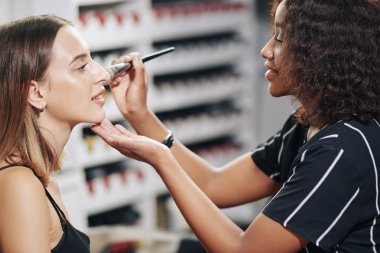 Makyaj sanatçısı yanaklarına pudra yüz hatları sürerken müşterisinden çenesini kaldırmasını istiyor.