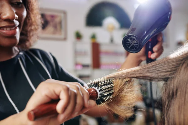 用圆形刷子和吹风烘干女性客户笑容发型师的特写形象 — 图库照片