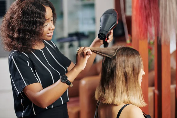 Gülümseyen Kuaför Genç Bayan Müşterinin Saçlarını Kurutuyor — Stok fotoğraf