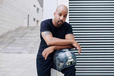 Kucağında motosiklet kaskına yaslanan yakışıklı, ciddi bir adam.