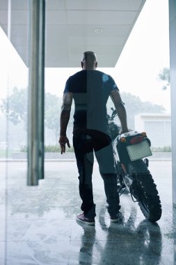 Yağmurlu bir günde motosikletinin yanında duran kendinden emin kaslı adamın dikiz aynası.