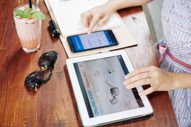 Young woman checking bank account via mobile app when searching for cheap sunglasses in online shop