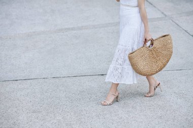 Beyaz dantel etekli genç bir kadının kesilmiş görüntüsü. Sokakta büyük bir saman torbasıyla yürüyor.