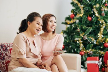 Gülen Vietnamlı anne ve yetişkin kız evde televizyonda komik bir program izliyorlar.