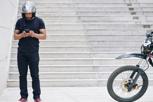 戴着摩托车头盔的男人站在室外发短信给朋友 — 图库照片