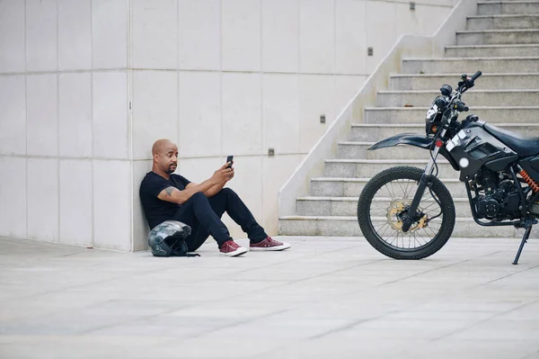 Muskulöser Mann Schwarzer Kleidung Sitzt Nach Motorradfahrt Auf Dem Boden — Stockfoto